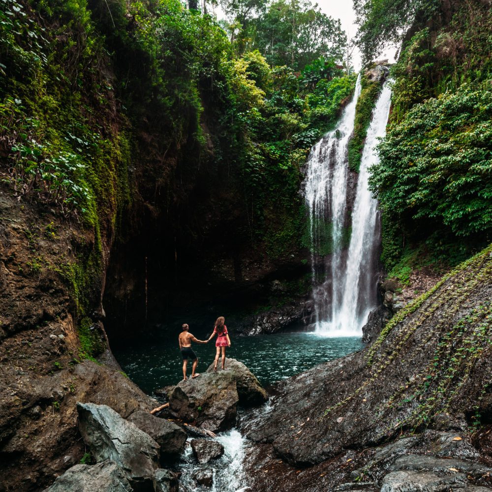 Lovers at the waterfall, rear view. Couple admiring a beautiful waterfall in Indonesia. Couple on vacation in Bali. Honeymoon trip. The couple is traveling in Asia. Vacation on the island of Bali